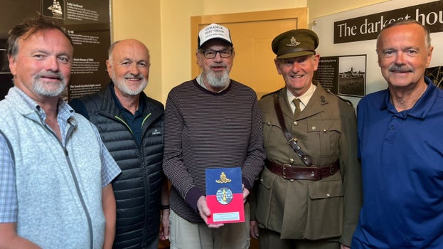 A group of people standing in a small room, one person is in military uniform, the person to his right is wearing a baseball cap with the words 'Strange but True' and 'Happy Birthday Don'